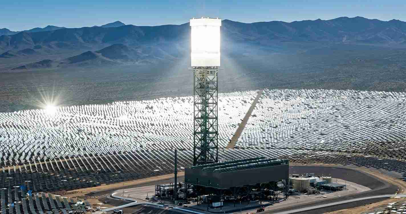 Solar power plant with a tall metal tower and long rows of solar panels in a desert landscape