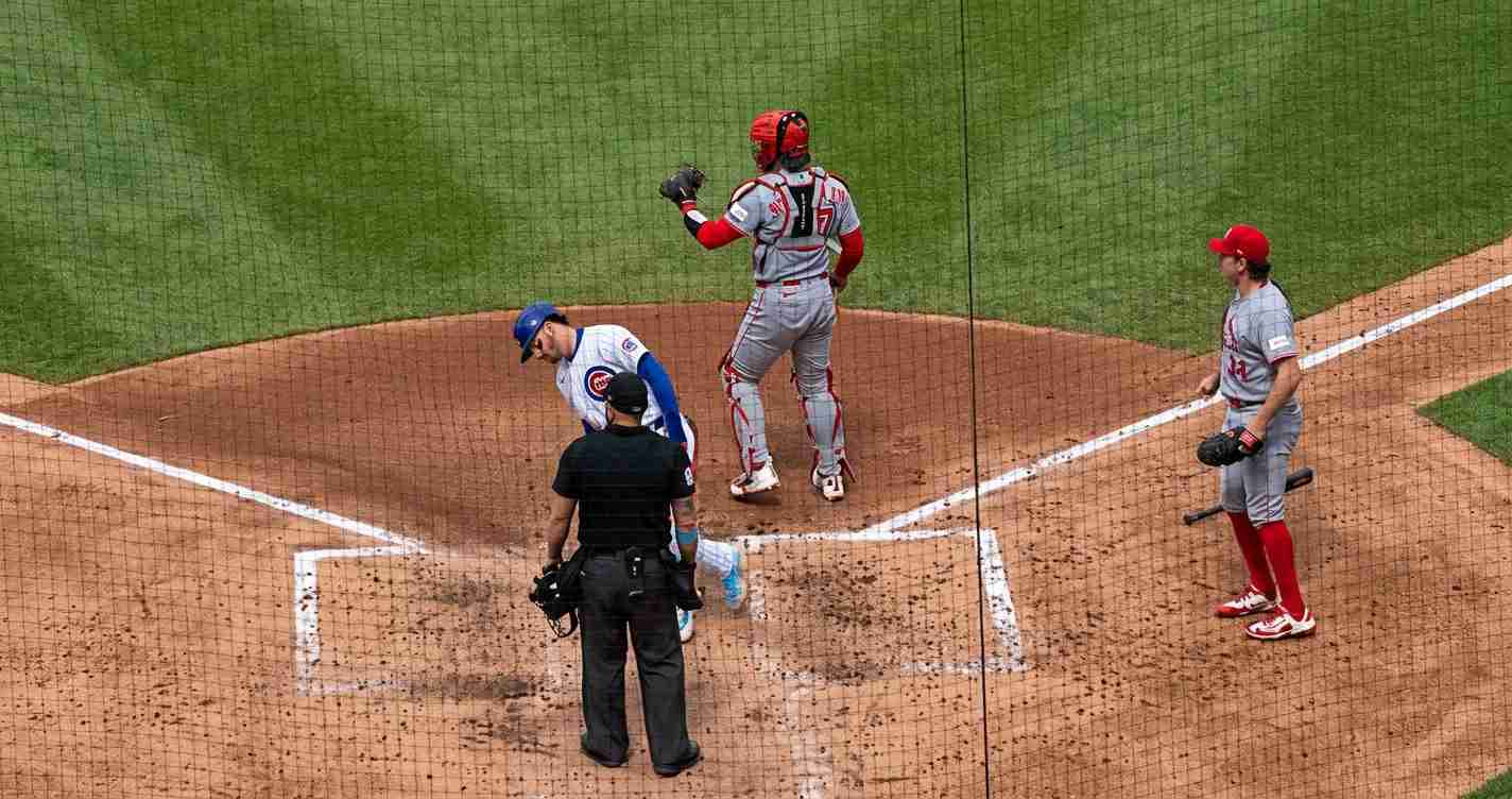 Baseball play at home plate: umpire in black checks the runner as a batter in blue helmet and a gray-catcher with red gear stand nearby.