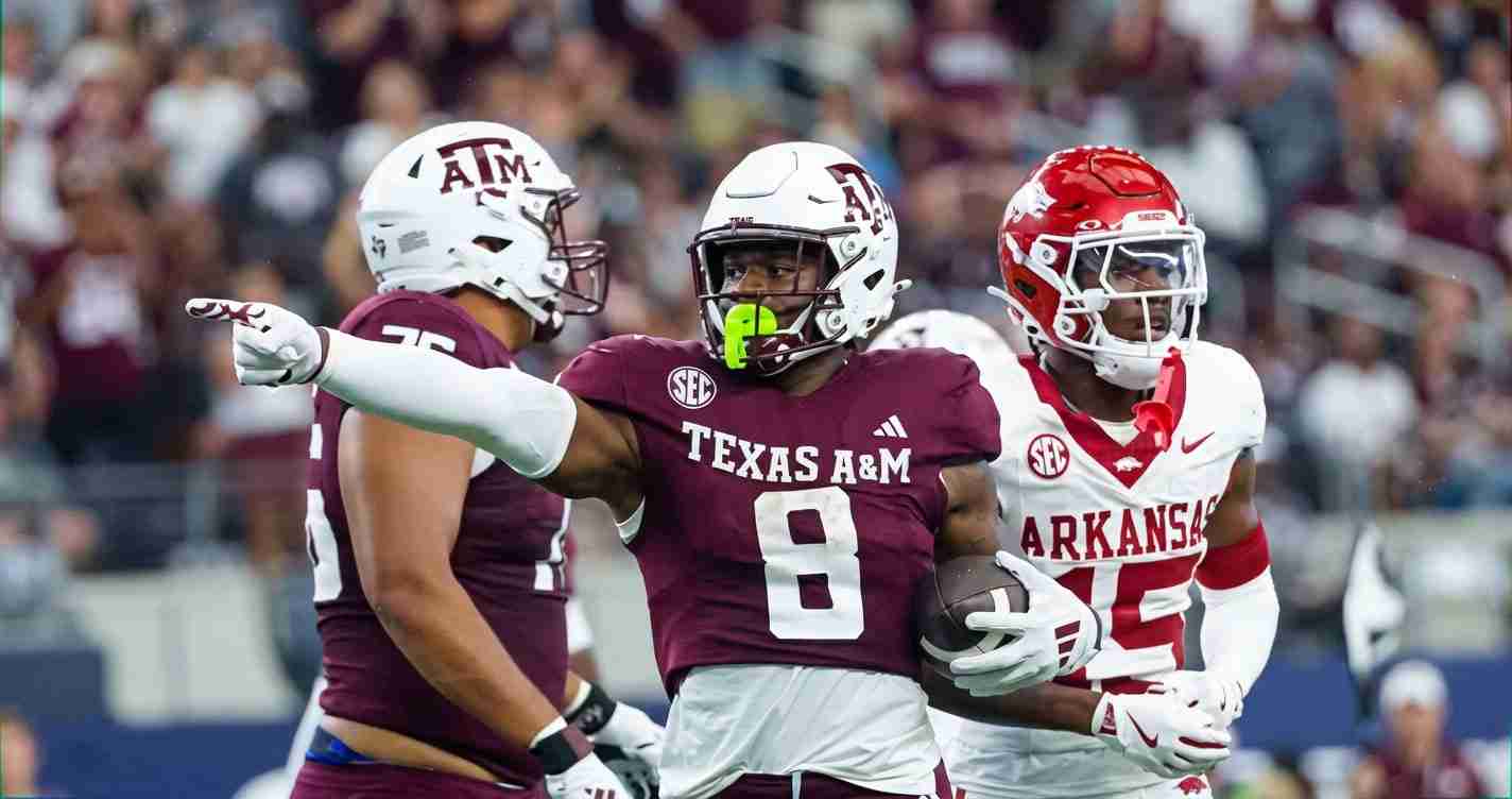 Texas A&M running back (number 8) carries the ball while an Arkansas defender pursues in a college football game.