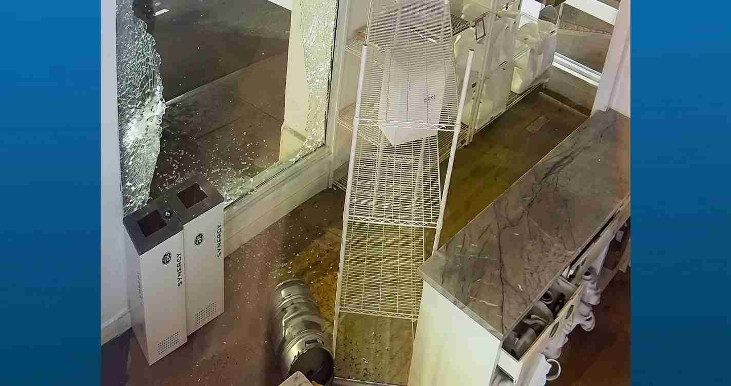 Storefront with a shattered glass window, toppled metal display rack, and scattered debris inside the shop floor.