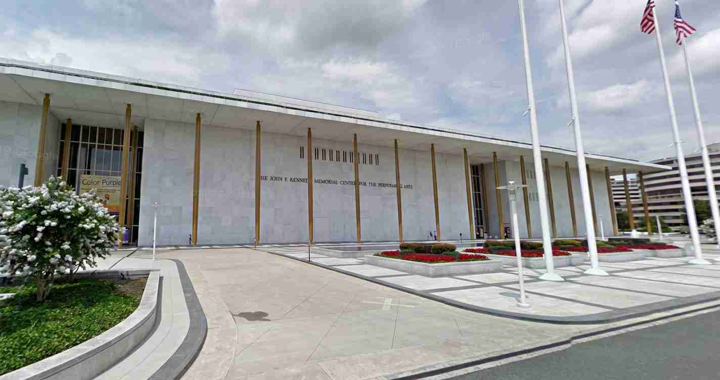 Front view of the John F. Kennedy Memorial Center for the Performing Arts with tall gold columns, flagpoles, and landscaped plaza.
