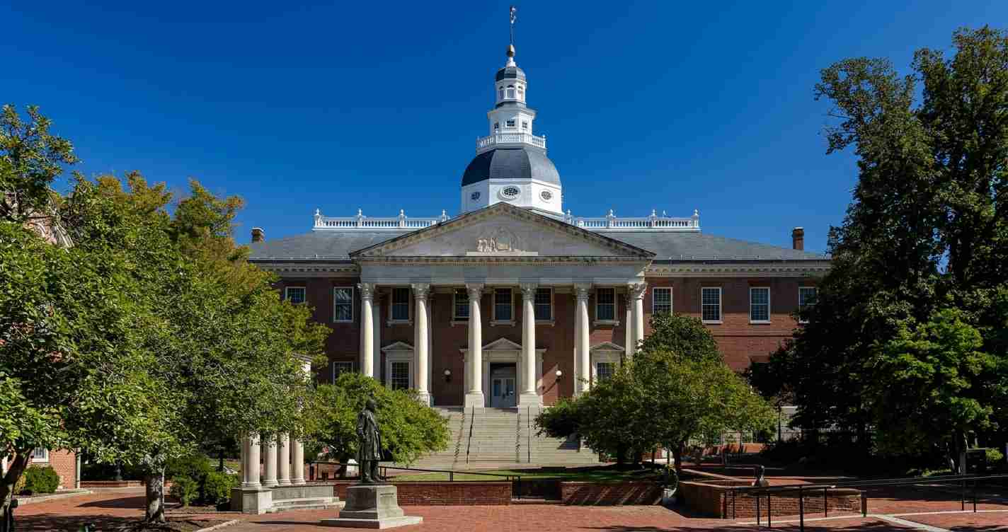 Front view of a neoclassical brick university building with tall white columns and a domed cupola under a clear blue sky.