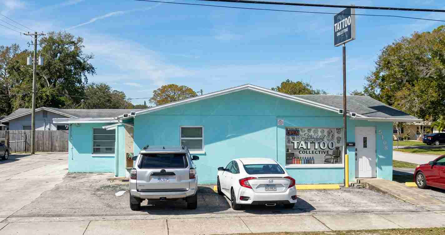 Turquoise tattoo shop with a large window sign reading 'Tattoo Collective' and two cars parked in front.