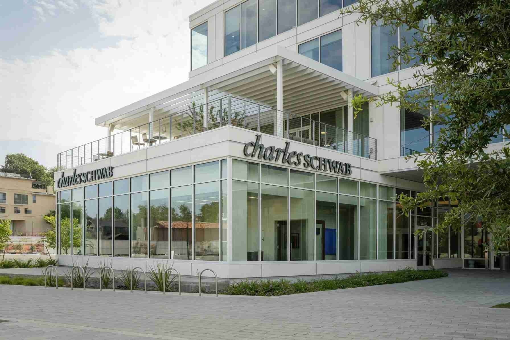 Modern glass office building with a Charles Schwab sign on the facade and a second-floor balcony on the left side.