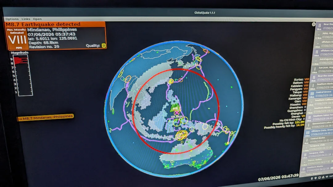 Earthquake monitor showing an M8.7 quake near Mindanao, Philippines, with a red epicenter ring around a 3D globe and status text on the left panel.
