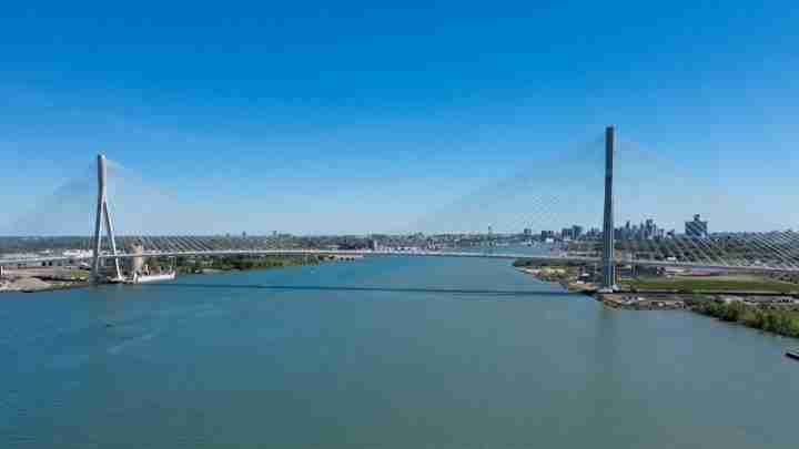 Aerial view of a cable‑stayed bridge crossing a wide river with a city skyline in the distance on a clear day.