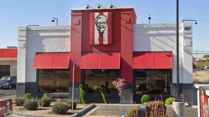KFC fast-food restaurant exterior with red curved awnings and Colonel Sanders logo above the entrance on a red facade