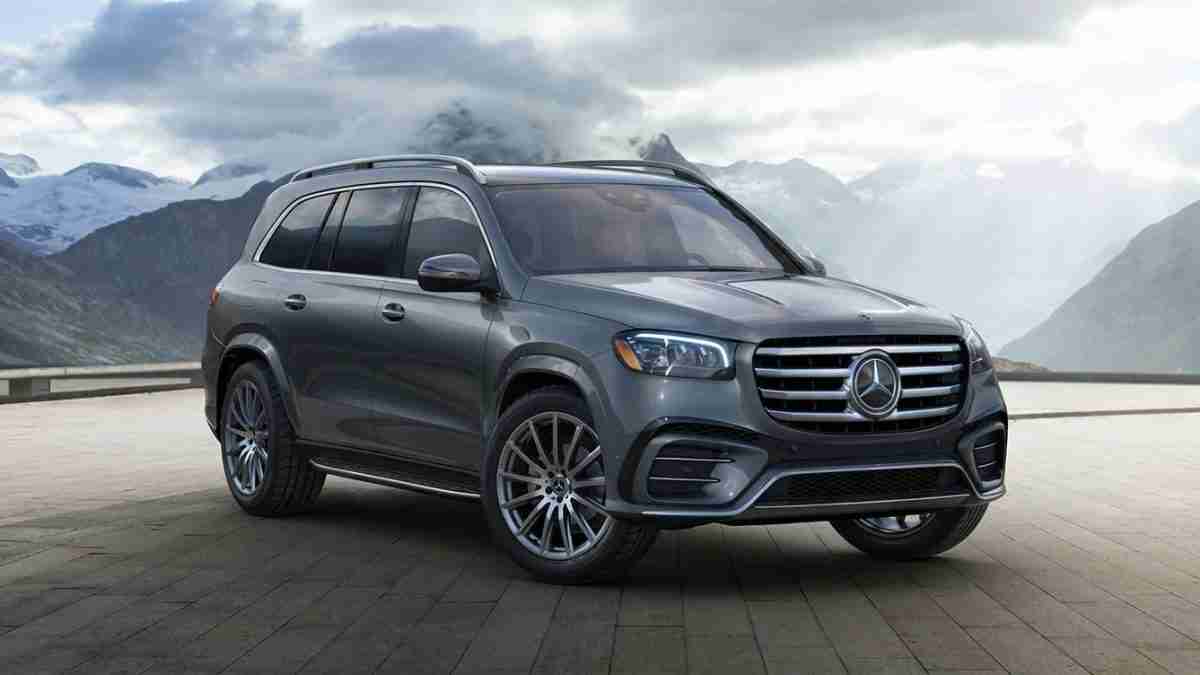 Grey Mercedes-Benz SUV parked on a mountain overlook with snow-capped peaks in the background, cloudy sky above.