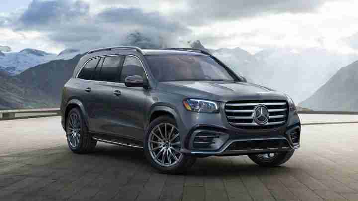 Grey Mercedes-Benz SUV parked on a mountain overlook with snow-capped peaks in the background, cloudy sky above.
