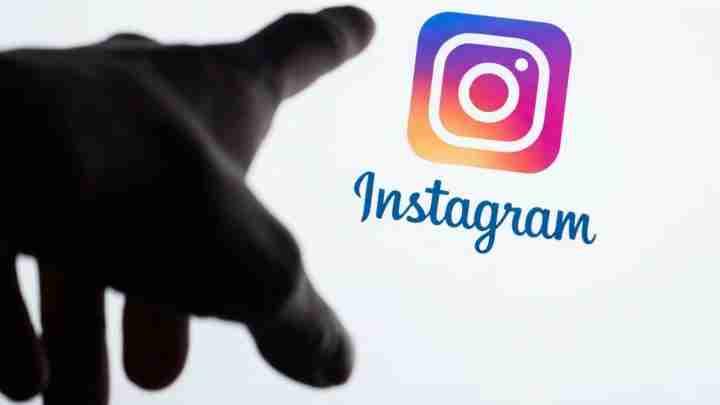 Outstretched hand reaching toward the Instagram logo and word Instagram, suggesting social media access or interaction.