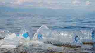 Plastic pollution: a large plastic bottle and scattered bags floating on calm water surface.