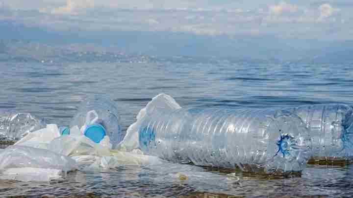 Plastic pollution: a large plastic bottle and scattered bags floating on calm water surface.
