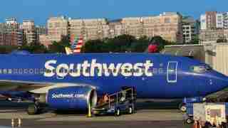Southwest Airlines jet at a gate with boarding stairs and ground crew nearby as buildings rise behind the terminal.