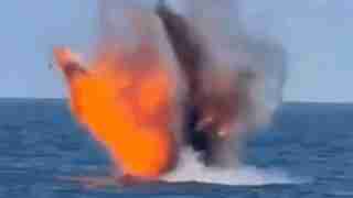Ocean scene showing an explosion at the surface with a bright orange fireball, dark smoke, and water spray around the impact point.