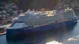 Cruise ship Celebrity APEX docked in a harbor beside a hillside town