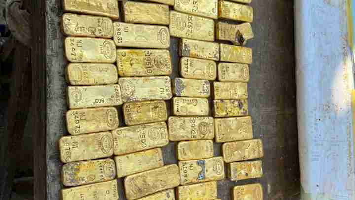 Row of gold bullion bars stacked on a wooden surface inside a ship or crate.