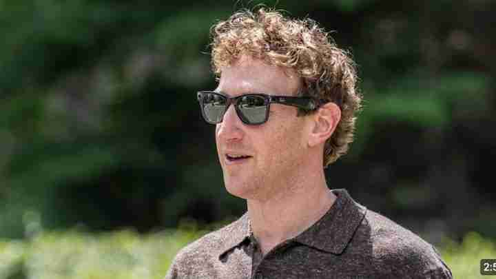 Man with curly blond hair wearing dark sunglasses outdoors, facing left.