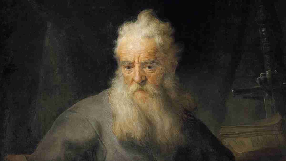 Portrait of an elderly man with a long white beard and solemn expression against a dark background, in a muted robe.